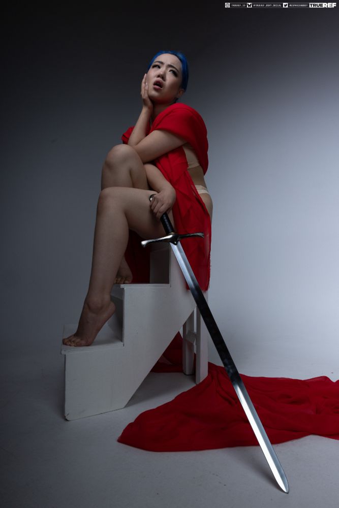Art pose reference of a woman sitting with a sword and draped in red fabric. 