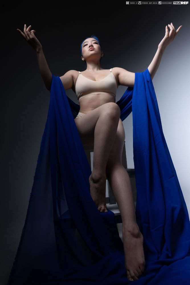 Art pose reference of a woman sitting with her arms out, draped in blue fabric. 
