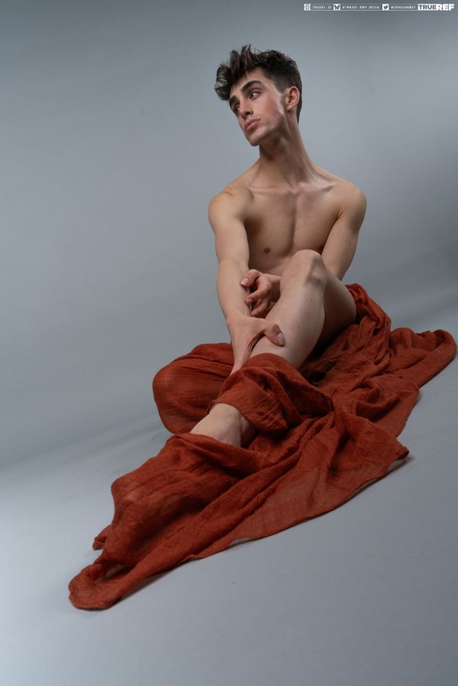 Pose reference of a man draped in red fabric, sitting on the ground.