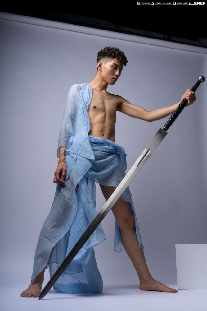 art pose reference of a young man draped in blue fabric holding a large sword. 