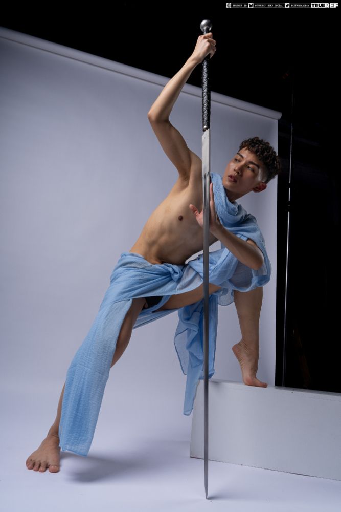 art pose reference of a young man draped in blue fabric holding a large sword. 