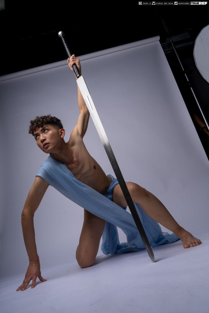 art pose reference of a young man draped in blue fabric holding a large sword. 