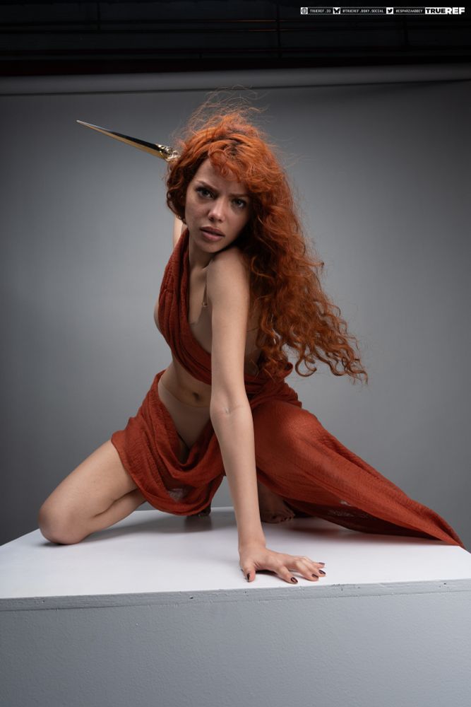 Pose reference of a woman draped in fabric crouching while holding a knife.  