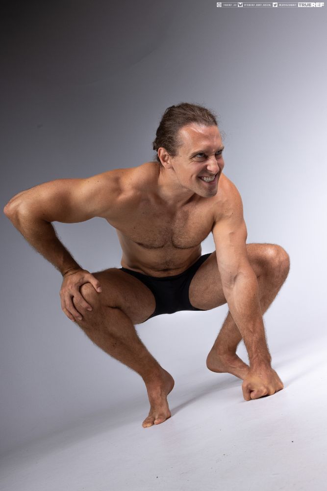 Art pose reference of a man crouching with a smile. 