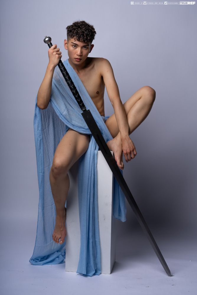 art pose reference of a young man draped in blue fabric holding a large sword. 