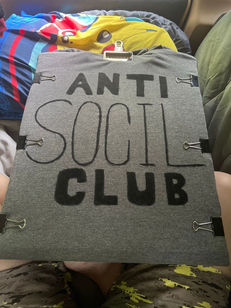 Photo of a shirt wrapped around some cardboard, so it is stretched out as much as it can be so I could then take some fabric markers and write “Anti Social Club” but now realizing I forgot the fucking A in social