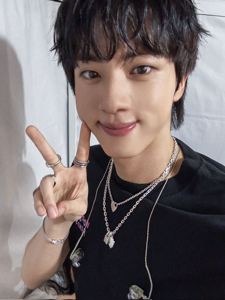 Seokjin selfie; he’s wearing black and holding up a peace sign