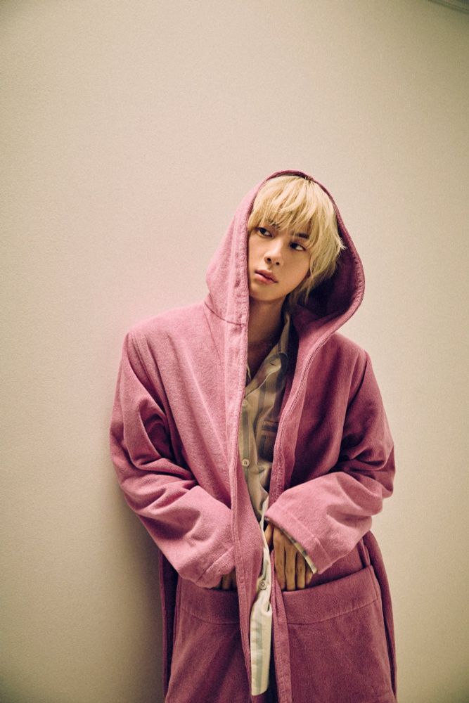 Blonde seokjin standing against the wall wrapped in his cozy pink robe