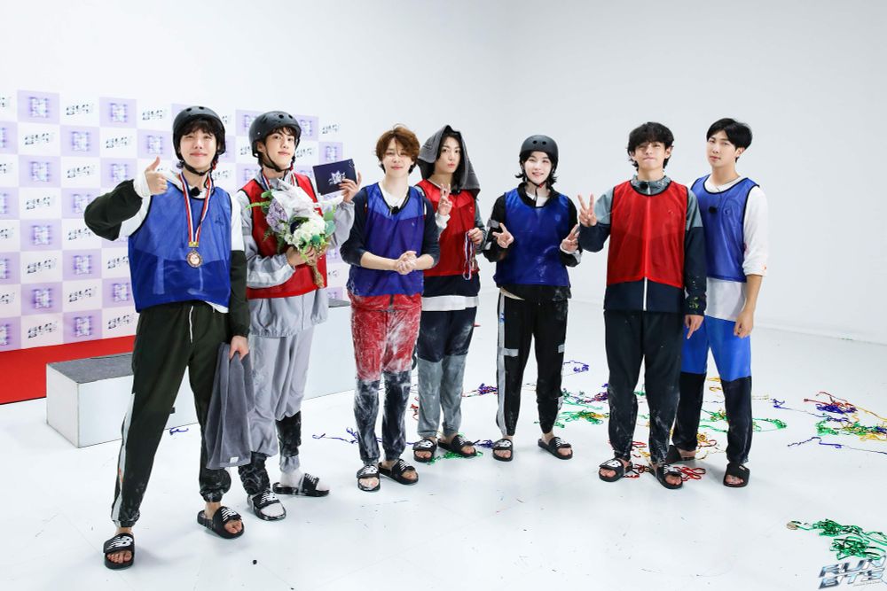 BTS posing in their blue and red active gears, some of them still wet from the football game. 