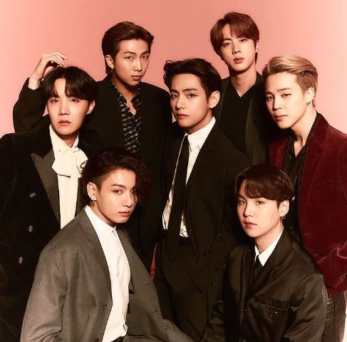 BTS dressed in black, grays and burgundy, in a room with warm lighting