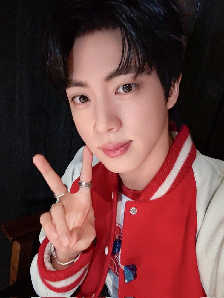 Seokjin in a red varsity jacket making a peace sign