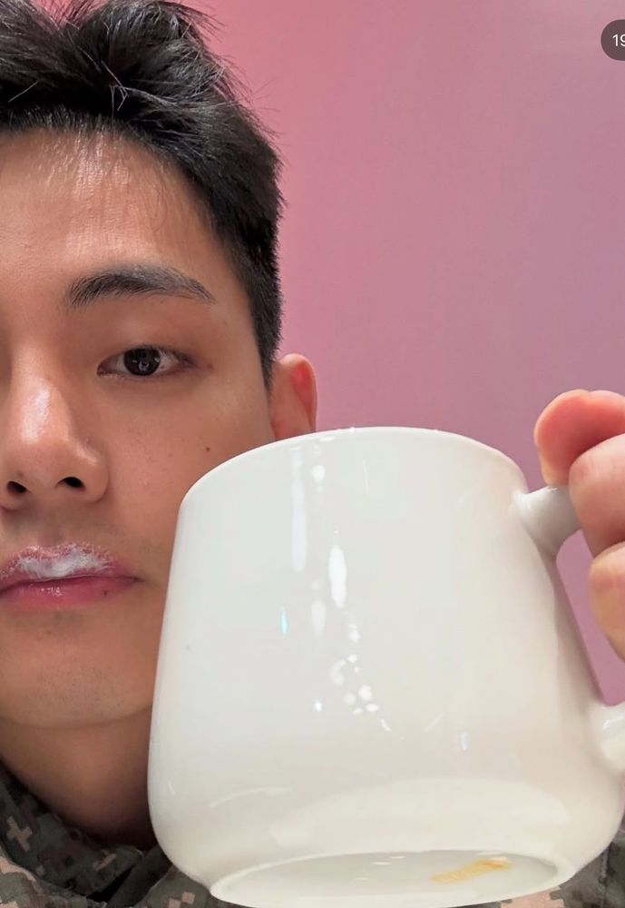 Taehyung with foam on his upper lip, holding a white mug