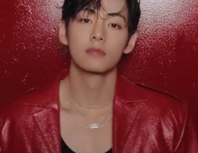 Taehyung in red leather jacket over black tanktop, leaning against a vibrant red wall