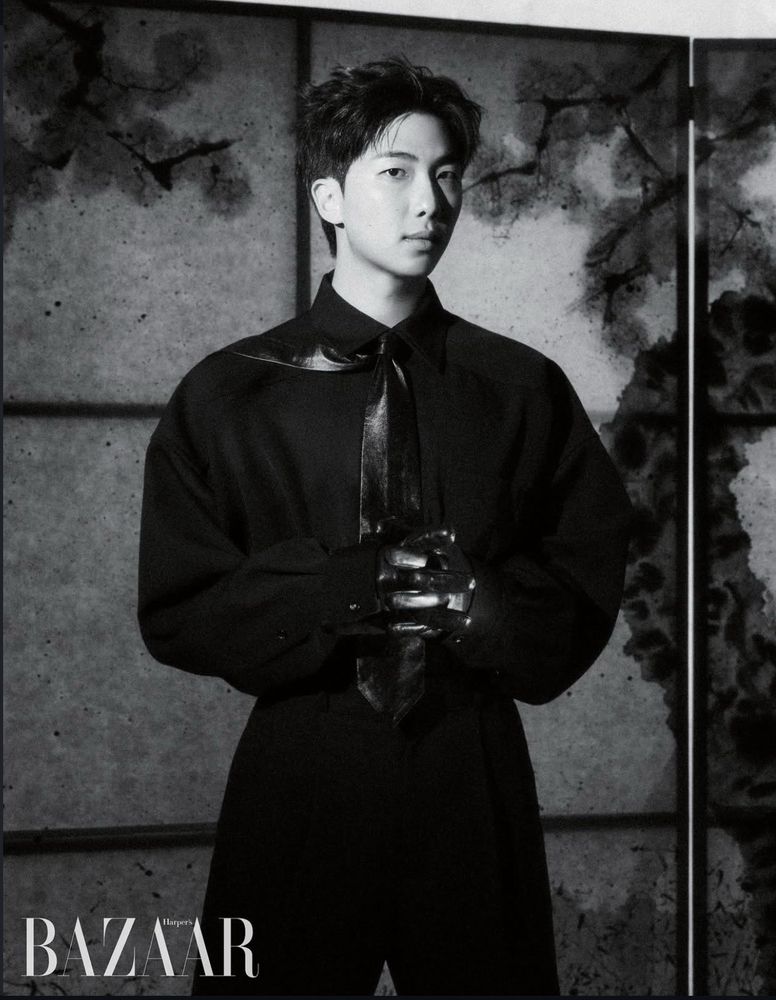 Black and White photo of Namjoon dressed in all black standing in front of a textured grid wall