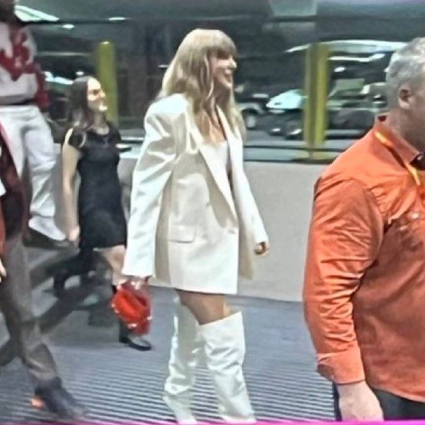 taylor swift arriving at superbowl wearing a white suit, white high boots and a red purse
