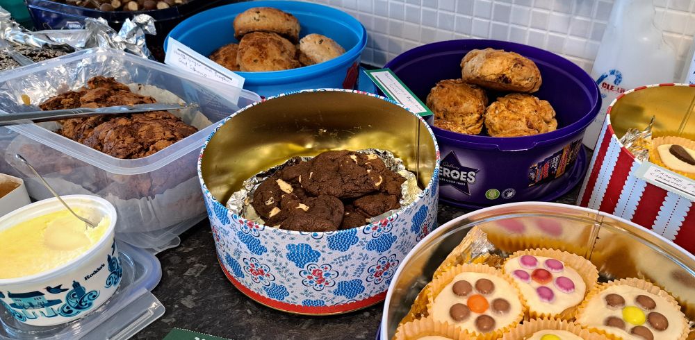Boxes full of homemade cakes. We can see chocolate cookies, 'smarties' fairy cakes, scones with cream, and apple cake.