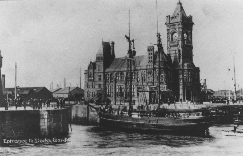 A black and white photograph take during the early-20th century showing a ship entering Cardiff's West Bute Dock, with the Pierhead Building in the background.