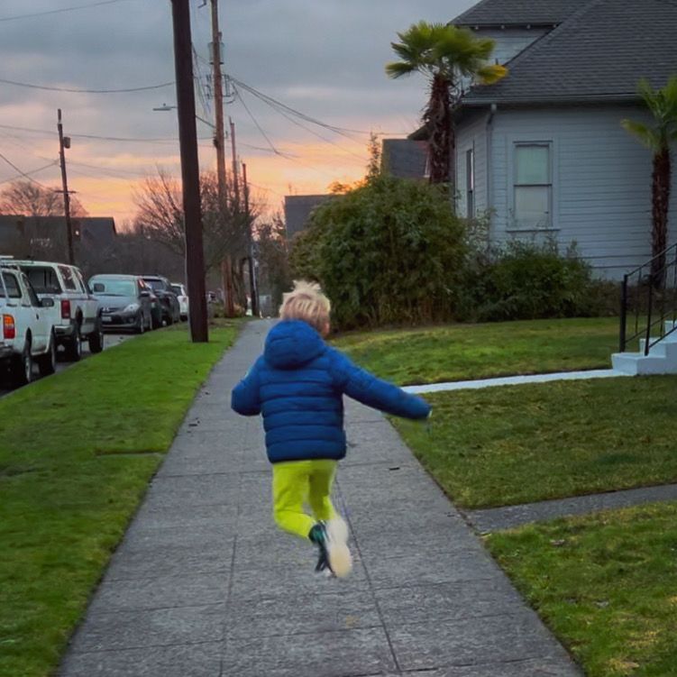 Boy jumping as he runs down sidewalk towards a beautiful sunset. 