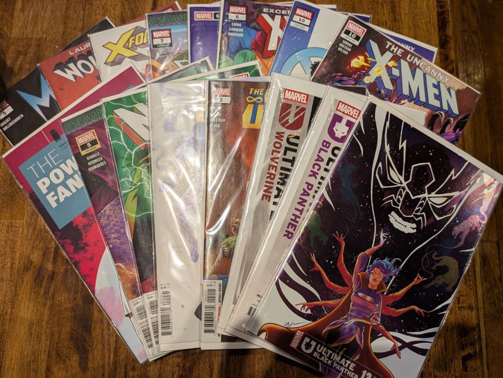A splay of a bunch of comic books (16 to be exact): Mystique, Laura Kinney: Wolverine, X-Force, X-Factor, Exceptional X-Men, Uncanny X-Men, Power Fantasy, Storm, NYX, Infinity Watch, and Ultimate Black Panther.