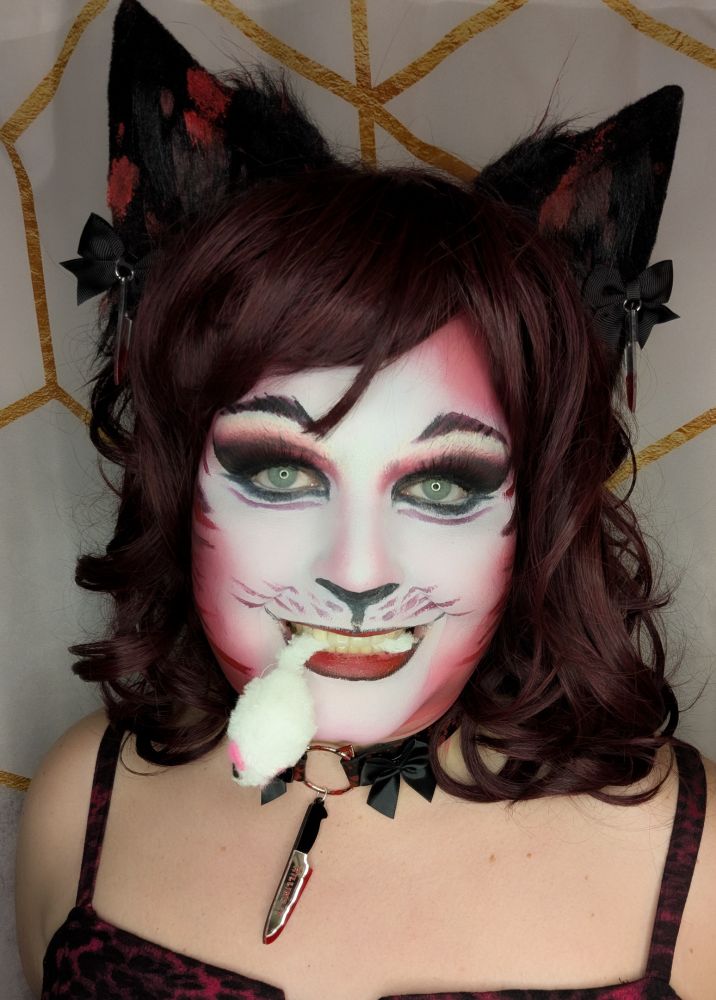 Selfie of Vivi in red and white Jellicle Cat style makeup with a white toy caught by the tail in her teeth.