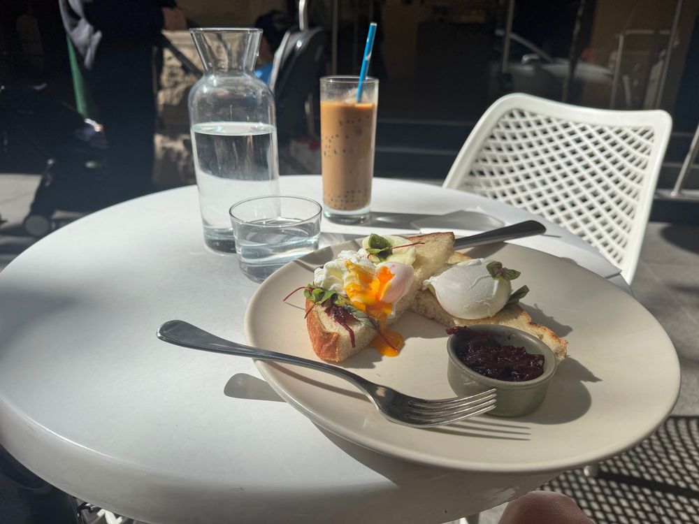 Boba coffee and a poached egg open face sandwich sit haphazardly on a white table 