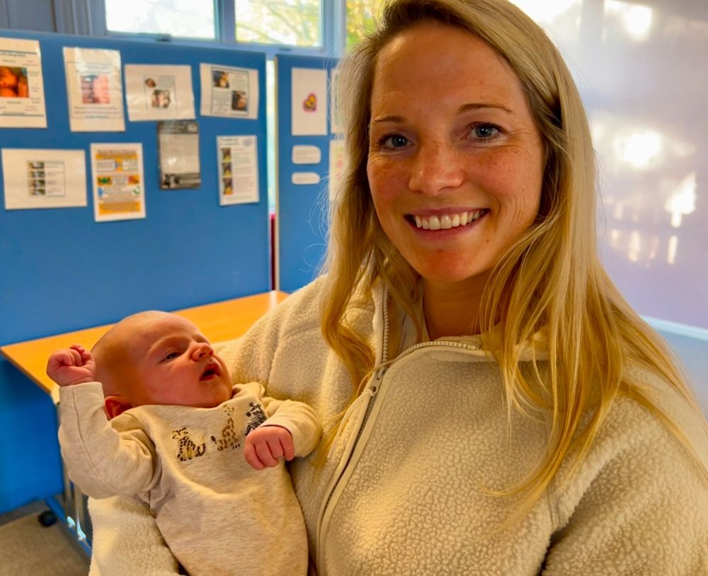 Woman with blonde hair, smiling, holding a baby