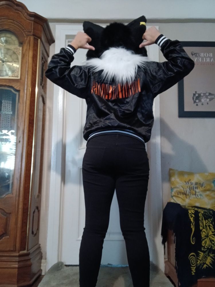 Black and white fursuit head facing away from the camera wearing a black and red varsity jacket with the Twenty One Pilots block text logo on the back