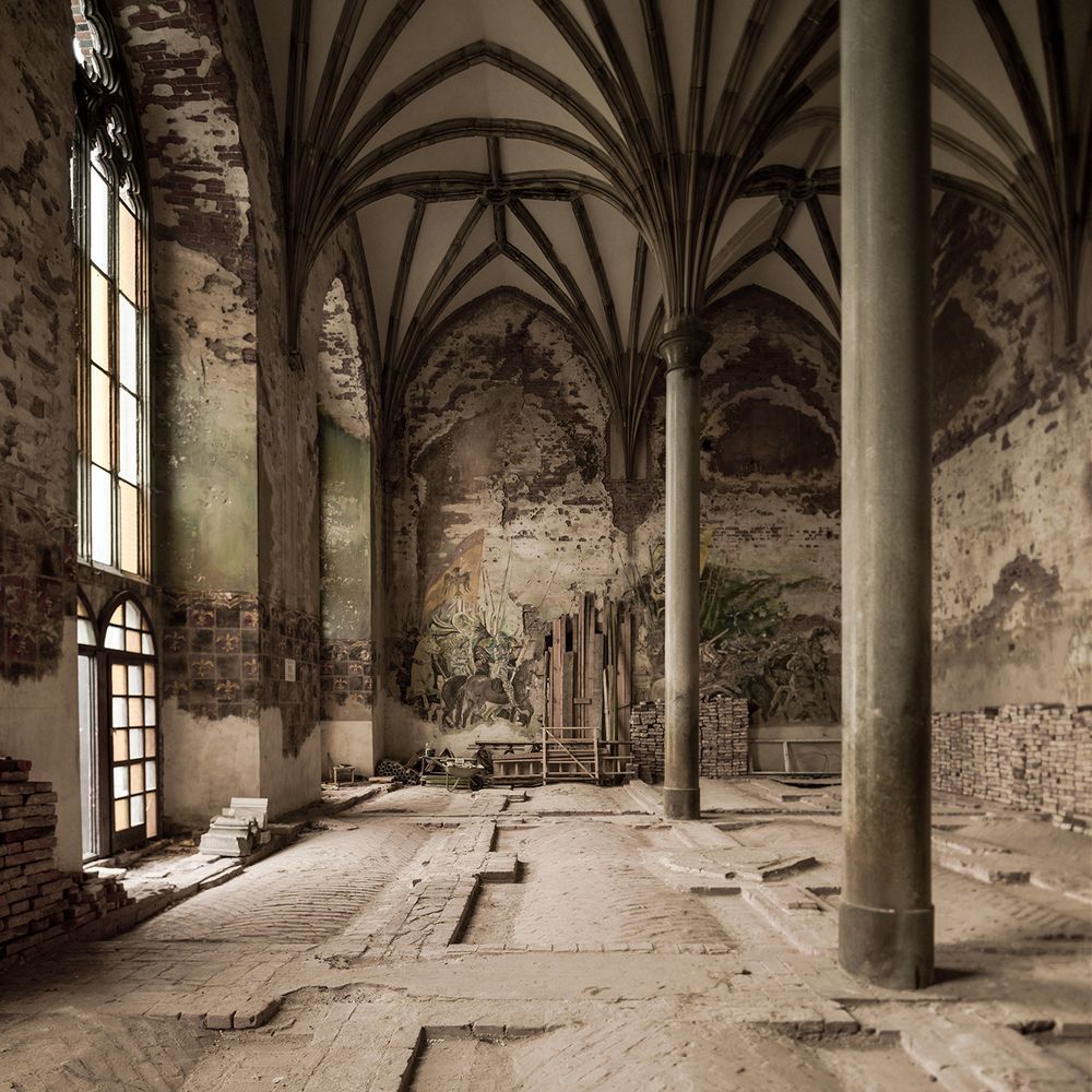 An abandoned sacred building space with arched ceilings and tall columns and patenaed brick walls and floors.