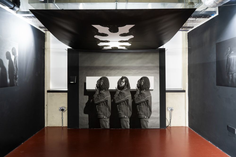 Exhibit from Yvann Zahui, MA Photography featuring three figures surrounded by photographic works.