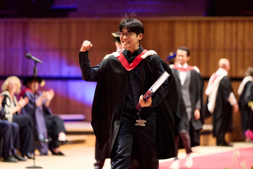 Student in graduation dress raises fist on stage.