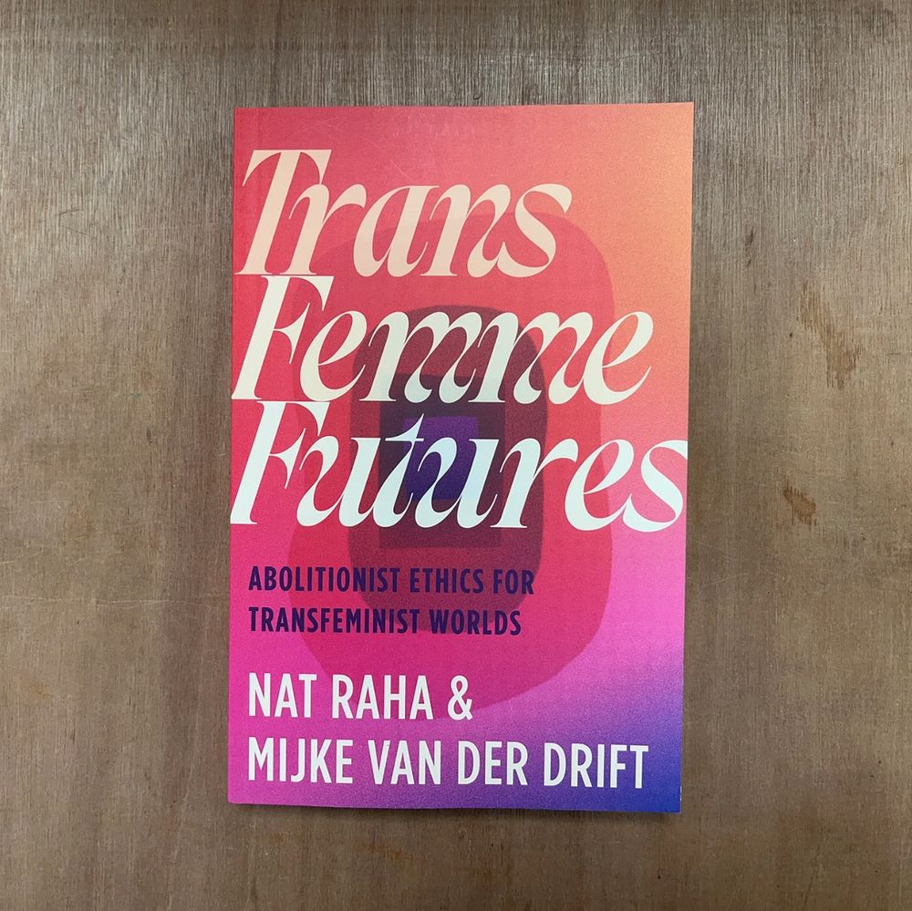 A book titled "Trans Femme Futures: Abolitionist Ethics for Transfeminist Worlds" by Nat Raha & Mijke van der Drift, displayed on a wooden surface. The cover features bold text in pink and blue gradients.
