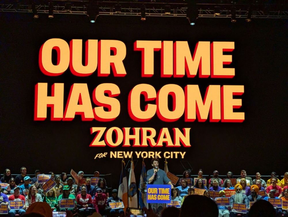 Photo of Gianmarco Soresi standing in front of a sign that says OUR TIME HAS COME
