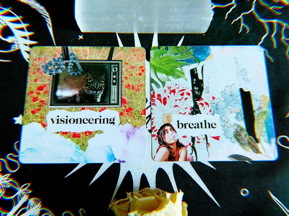 Two collage style cards square cards with a selenite stick above them and a dried yellow rose underneath. 

The card on the left shows an upside down old-style television in a field of red poppies with a tabby cat on the screen and a snake winding around on one of the legs. The word "visioneering" is featured. 

The card on the right shows a woman blowing bubble gum while looking up; the background shows a door open ajar with a black lace bra hung over it. There are house plant leaves and a lace parasol on the frame. The featured word here is "breathe."