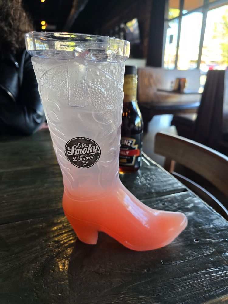 a photo of a small(ish) clear plastic boot full of a gradient beverage going from clear at eye top to pink on the bottom- a small decal on the side reads "Ole Smoky Distillery"