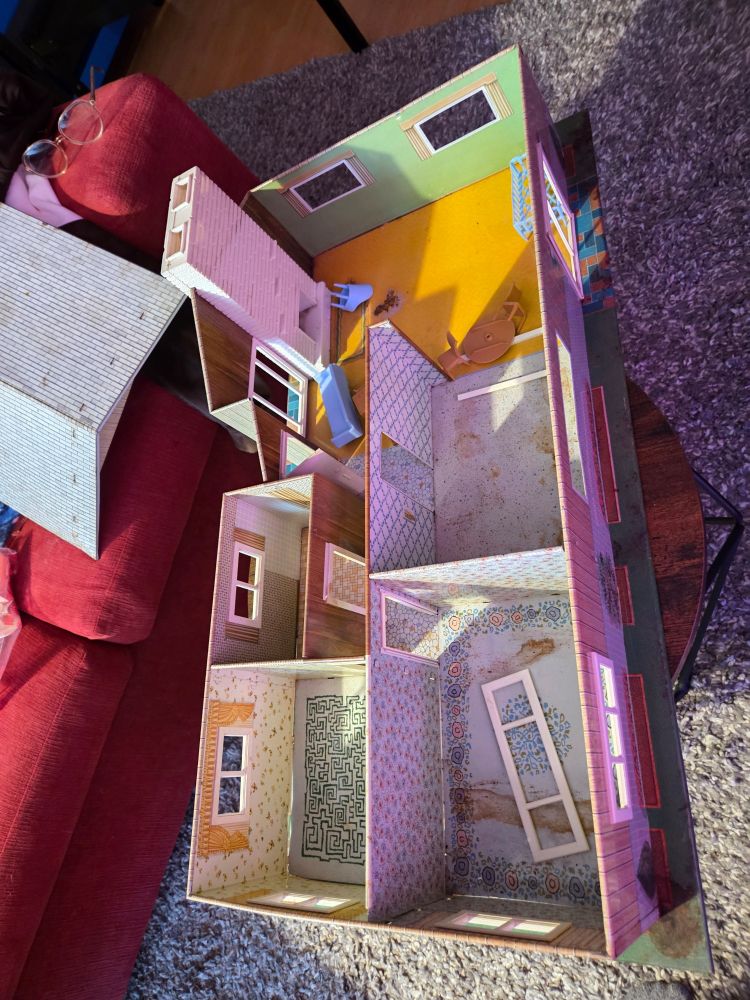 Ranch style tin house on a small table in a living room with the roof lifted off revealing all the little rooms in 1960s decor