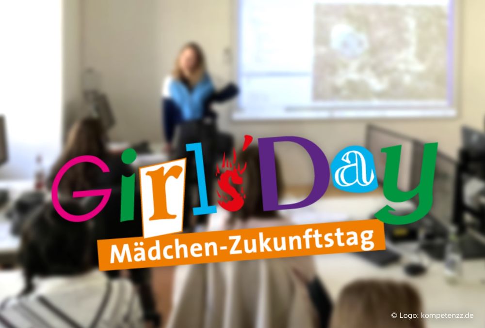 Girls'Day logo on blurred background picture of a pc-pool exercise with multiple students