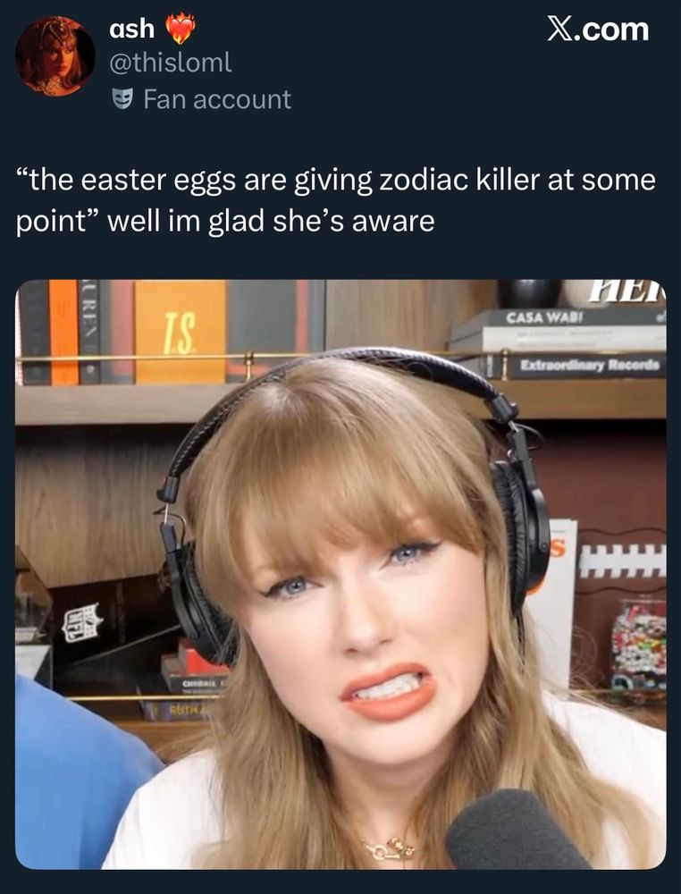 This image is a cropped screenshot of a tweet from the user “ash” (@thisloml, marked as a Fan account) on X.com. The tweet reads: “the easter eggs are giving zodiac killer at some point” well im glad she’s aware. Below the tweet is a close-up photo of Taylor Swift wearing large, black over-ear headphones and a white top. Her long blonde hair is styled with bangs, and she has bright red-orange lipstick. Taylor is making a humorous, slightly awkward grimace, showing her teeth in a crooked smile, as if reacting playfully or with mock discomfort. Behind her is a blurred background of wooden shelves holding various books and décor items, including a black-and-white object shaped like a football, a “CASA WABI” book, and another labeled “Extraordinary Records.” The image gives the impression of a playful, inside-joke moment connecting Swift’s habit of hiding cryptic “easter eggs” with the elaborate codes of the Zodiac Killer.