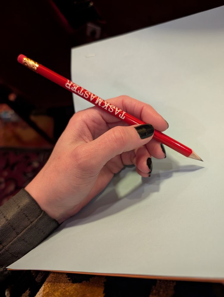 A photo of a hand holding one of the red Taskmaster pencils that were handed out to the audience, demonstrating that if you happen to be left-handed, your pencil will read upsidedown. Rude. I've got hurt feelings.