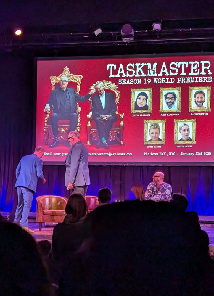 Greg and Alex on stage taking their seats next to host Josh Gondelman