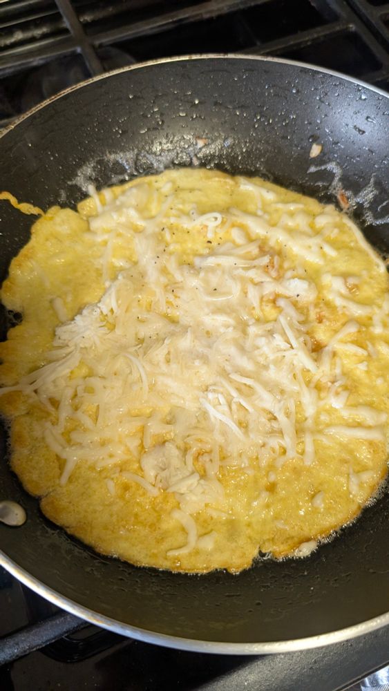 Eggs in skillet with shredded mozzarella cheese added.