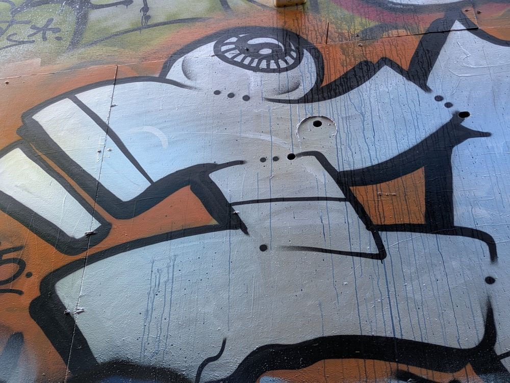 Art painted on wall, white shape that looks like a sideways H with an eyeball on top, outlined in back, on reddish-brown background