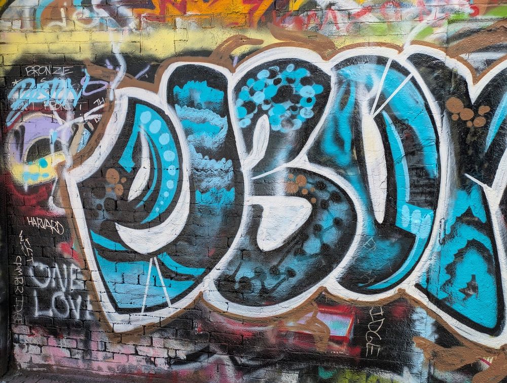 Spray painted tag on wall, large stylized lettering with blue & black gradient designs inside.  "One Love" painted lower left.