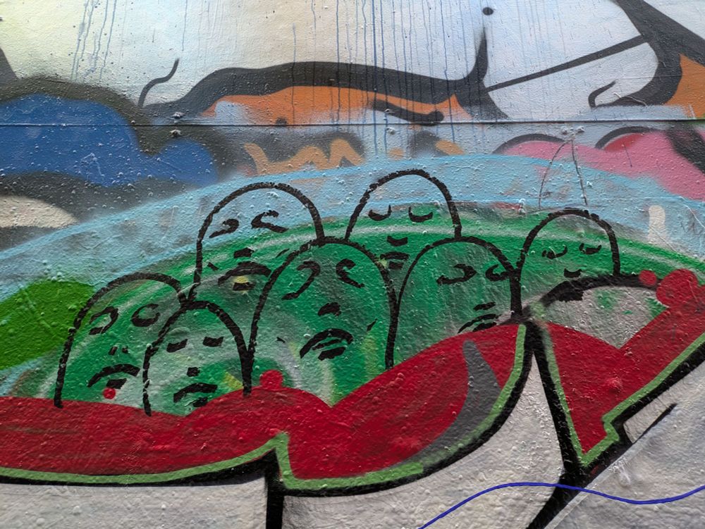 Graffiti art on wall - outlined abstract heads with faces on green & blue background with colorful shapes below