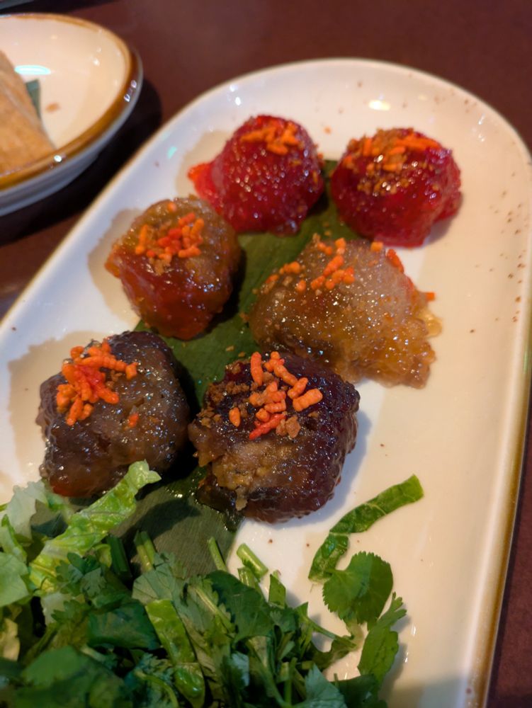 Six shiny food lumps in three different colors on a long plate with orange garnish bits on top 