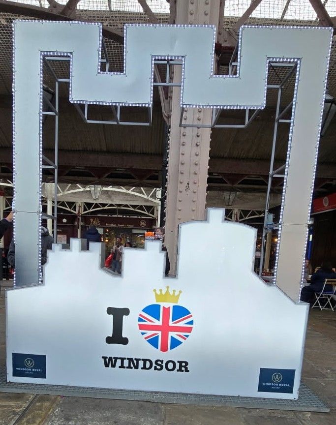 Orange Roumd Fox and Nui Limbus Heathcliff sitting on a little platform at this selfie looking station at Windsor Castle with the text under them saying "I heart Windsor" with the heart being the UK Flag with a yellow crown above it.