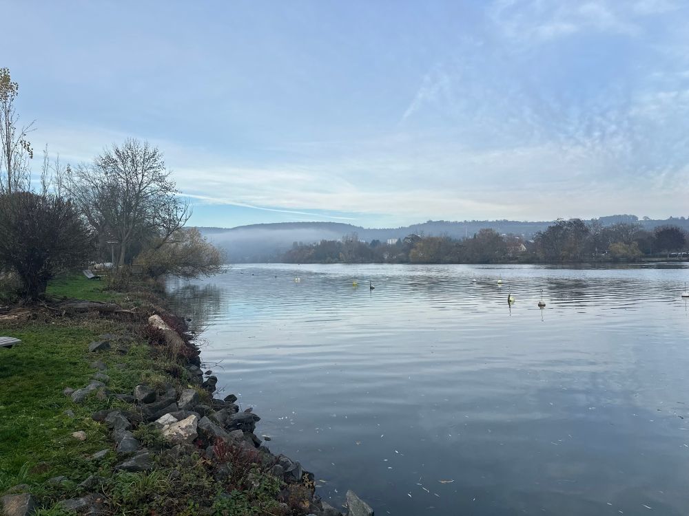 Blick auf einen Fluß, der sehr ruhig in seinem Bett liegt. Die verschiedenen Blautöne der Wolken und des Himmels spiegeln sich im Wasser. Dieses Bild wurde vom linken Flußufer aufgenommen 