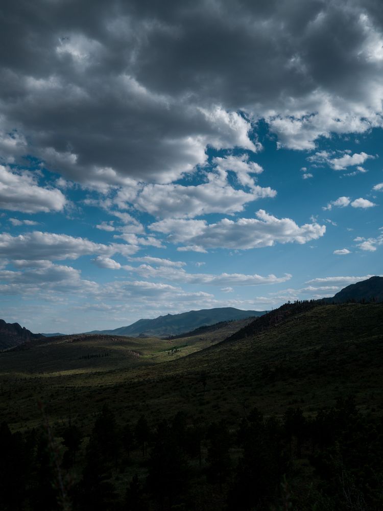 Rolling hills covered in shadows from the clouds above. This is creating a kind of spotlight effect on the landscape where the sun is breaking through