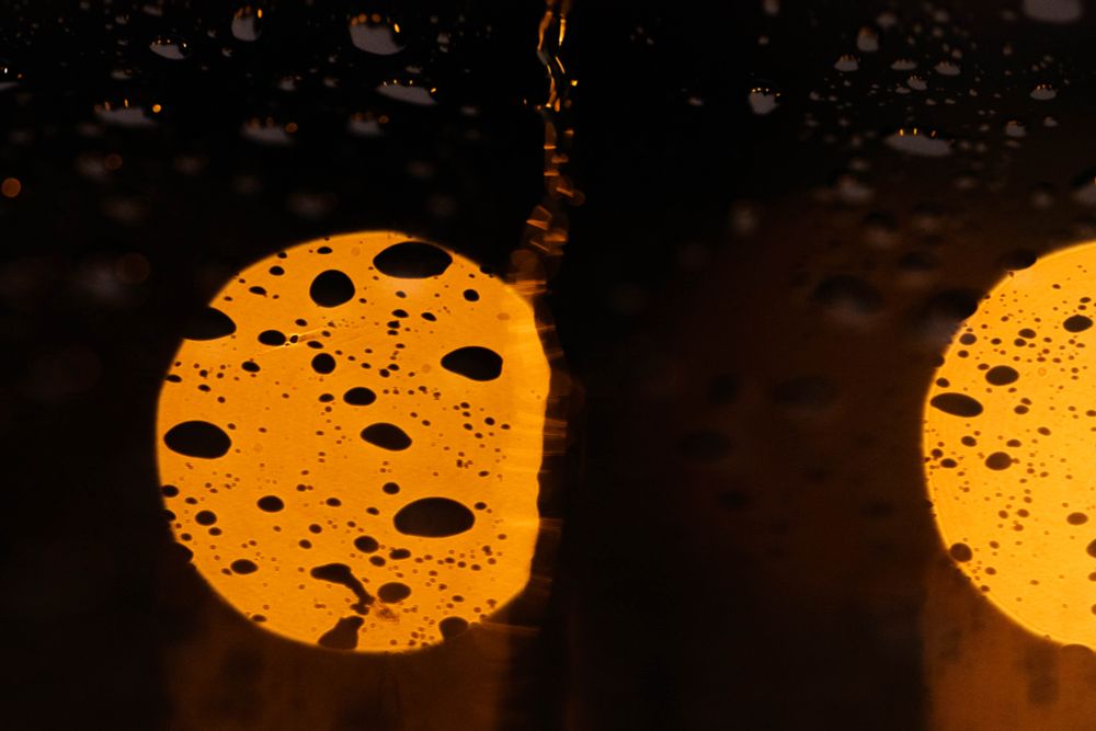Water flows on a windshield with bright orange lights as bokeh balls in the background