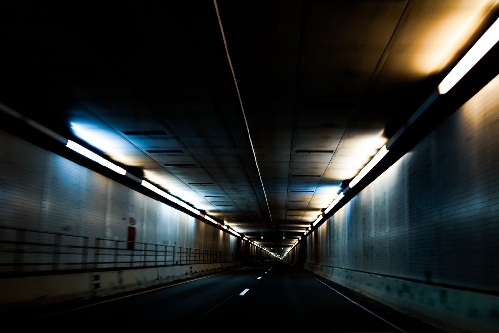 Dark photo of an empty highway tunnel with lights along the top