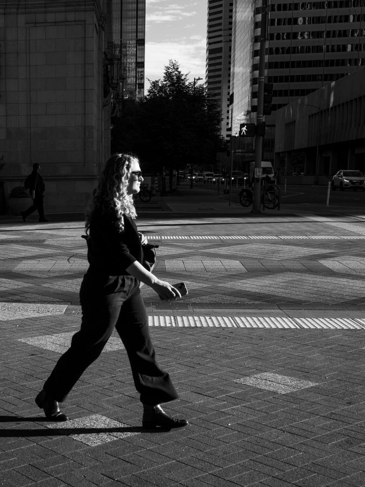 A woman walks on the sunny side of the street